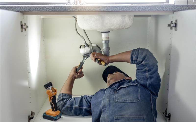 Plumber repairing pipes beneath a bathroom sink in Spring Hill