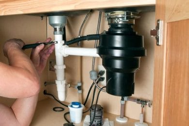 Plumber repairing a garbage disposal beneath a kitchen sink in Spring Hill