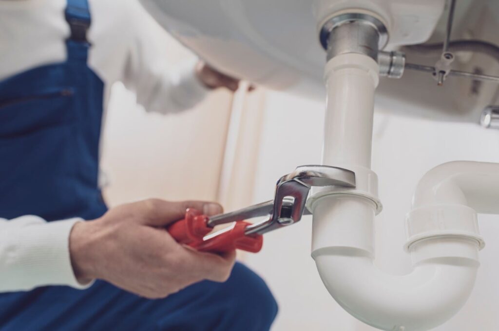 Plumber repairing a white drain pipe beneath a sink in Spring Hill